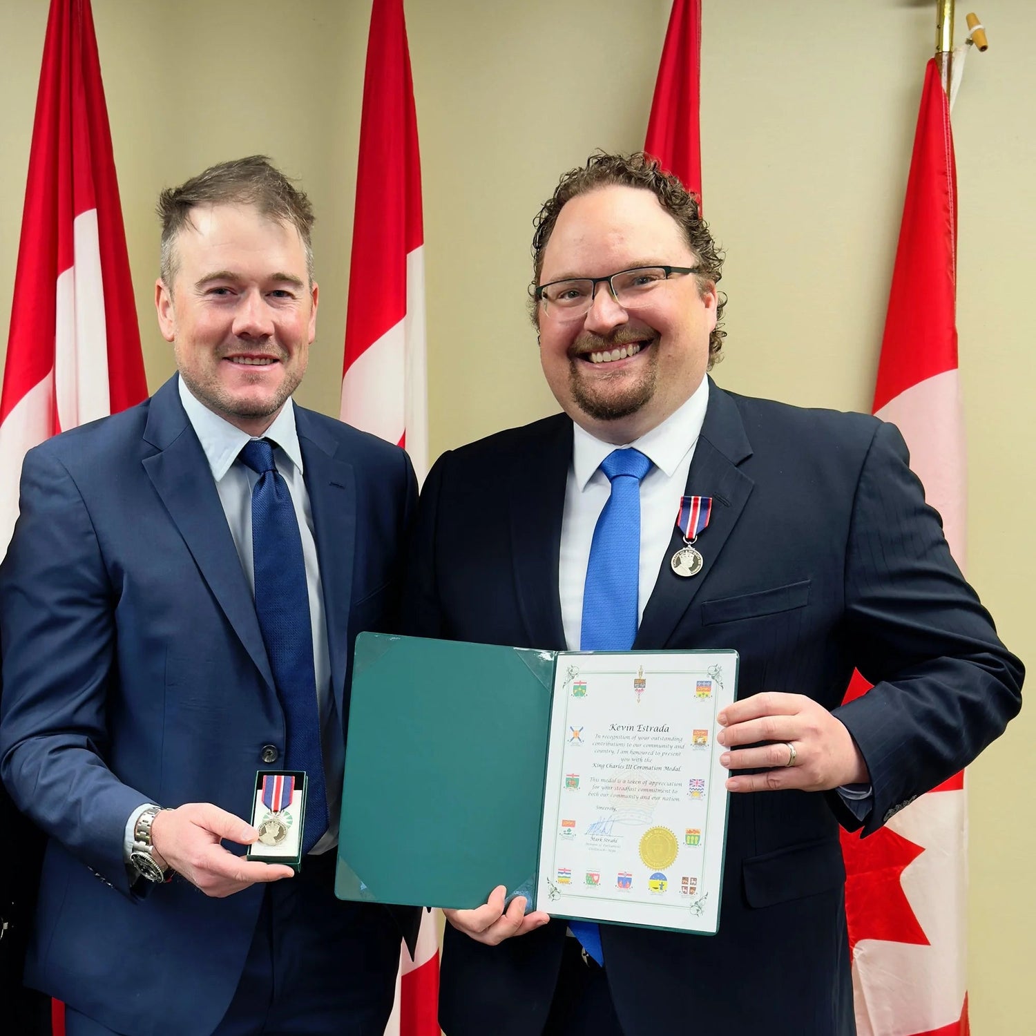 Two men in suits holding certificates in front of Canadian flags